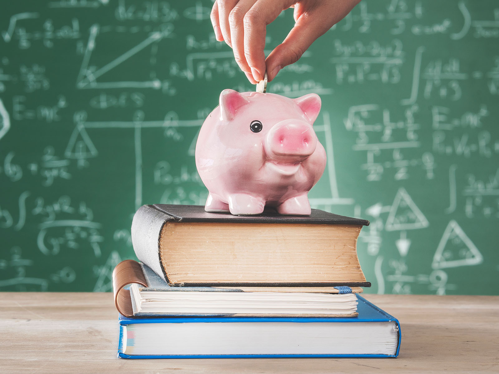 Hand putting coins into a piggy bank on top of textbooks