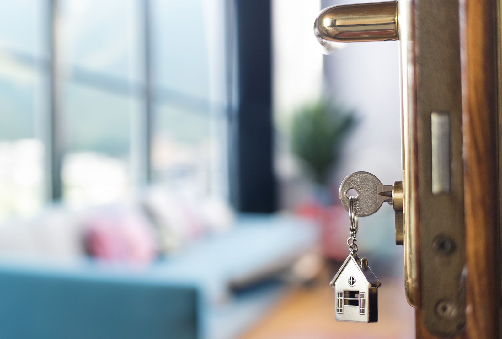 House-shaped keychain dangling from the lock of a door opened into a home
