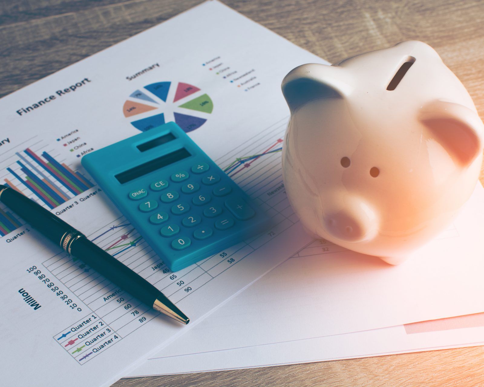 ] A piggy bank, pen and calculator resting on a financial report